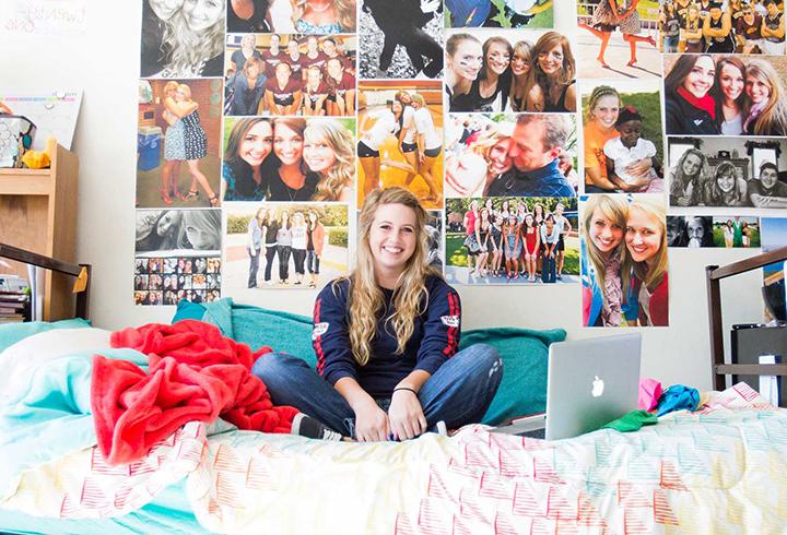 Student sitting on bed in dorm room